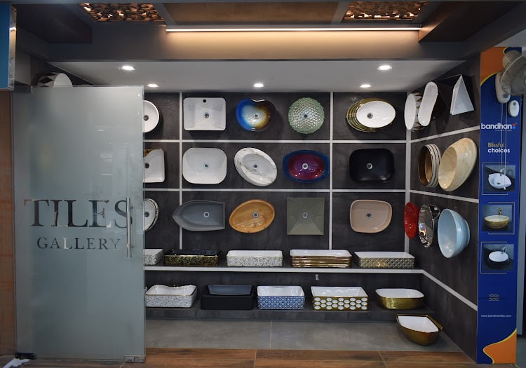 Coloured and patterned designer basins on the grey display wall beside the frosted-glass Tiles Gallery door