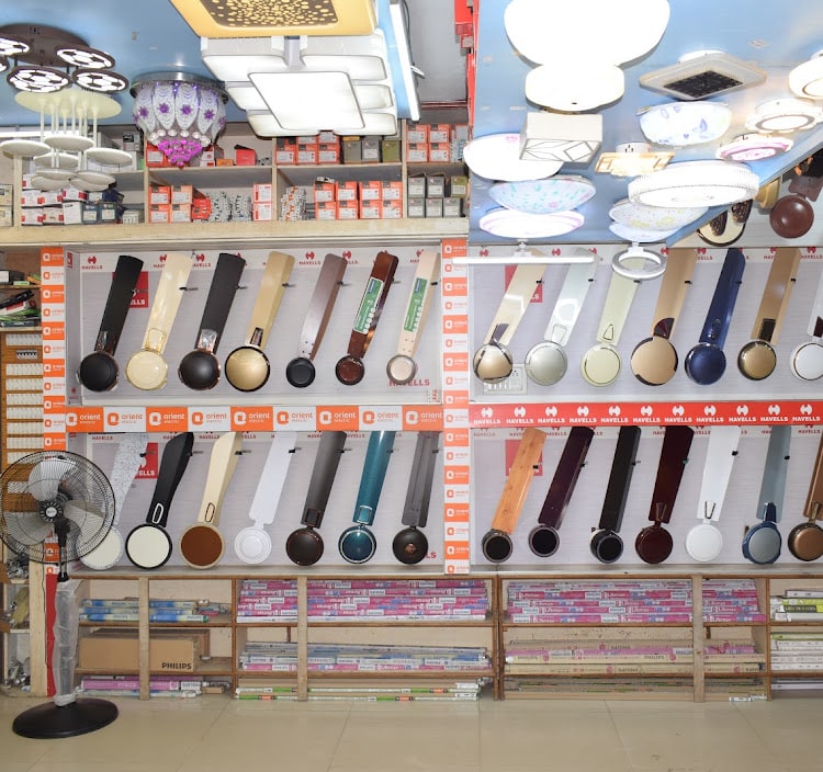 Havells and Orient ceiling fan blades in every finish mounted across the wall above shelves of tube lights