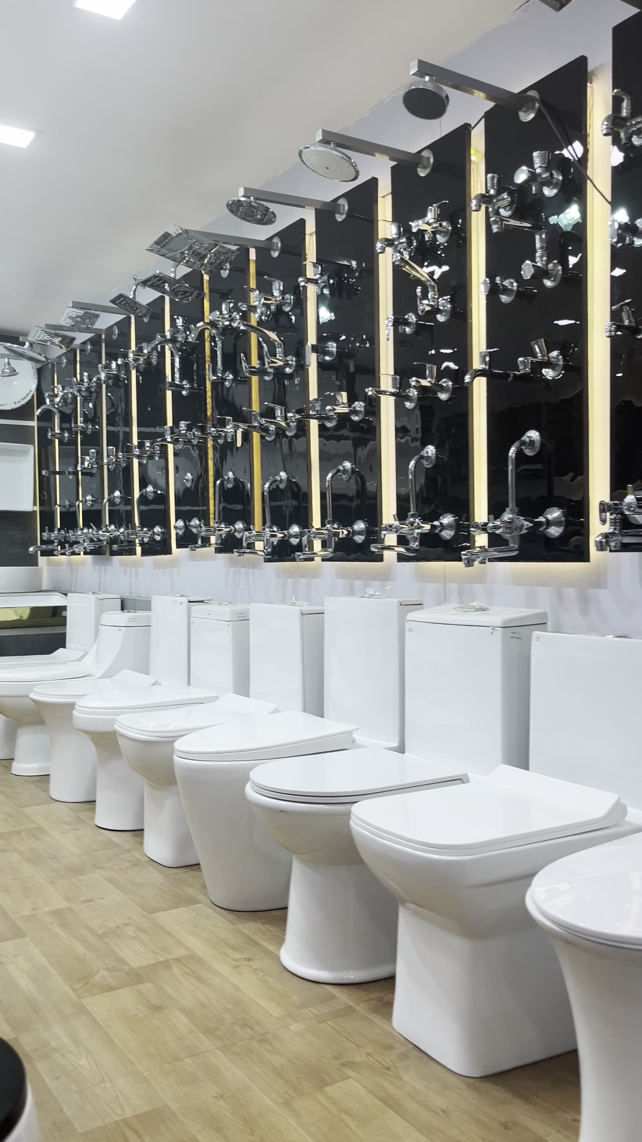 Row of one-piece and two-piece water closets on the showroom floor with the chrome fittings wall behind